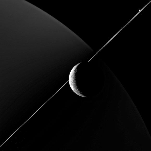  This image of Dione was taken with the wide-angle camera aboard Cassini on June 16, 2015. Also making an appearance in this image is Saturn’s moon Enceladus, seen in the upper right, just above the bright line of Saturn’s rings 